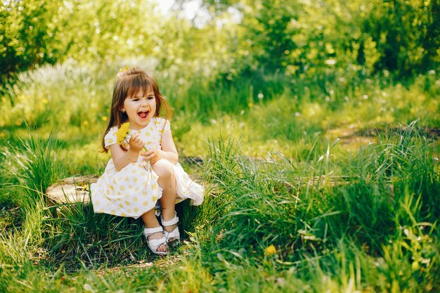 een klein meisje met prachtig lang haar en in een gele jurk speelt in het zomerpark