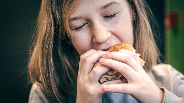 Gratis foto een klein meisje met sproeten eet een hamburger