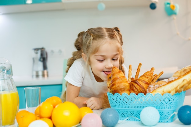 Een klein meisje ontbijt in de keuken met croissants en jus d'orange.