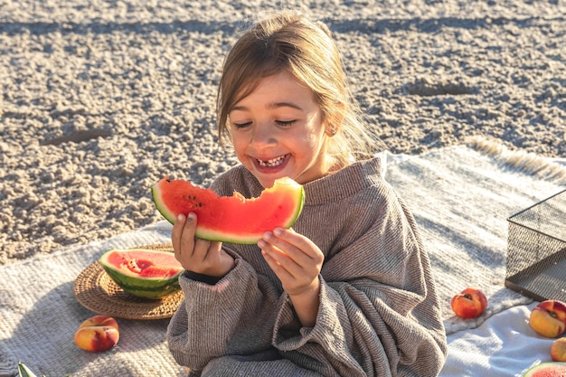 Gratis foto een klein meisje op een zandstrand aan zee eet een watermeloen