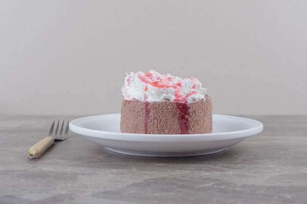 Een kleine cake met slagroom en aardbeiensiroop op een plaat op marmer