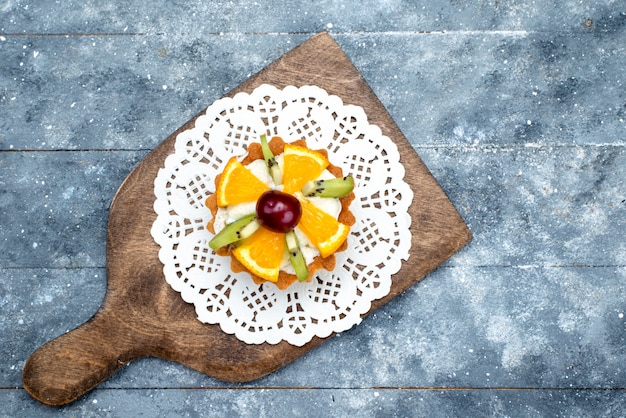 Een kleine heerlijke cake van bovenaf met room en vers gesneden fruit op het grijze koekje van de bureaufruit