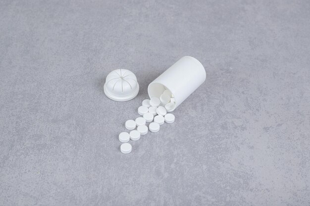 Een kleine witte pot met witte pillen op een grijze achtergrond.