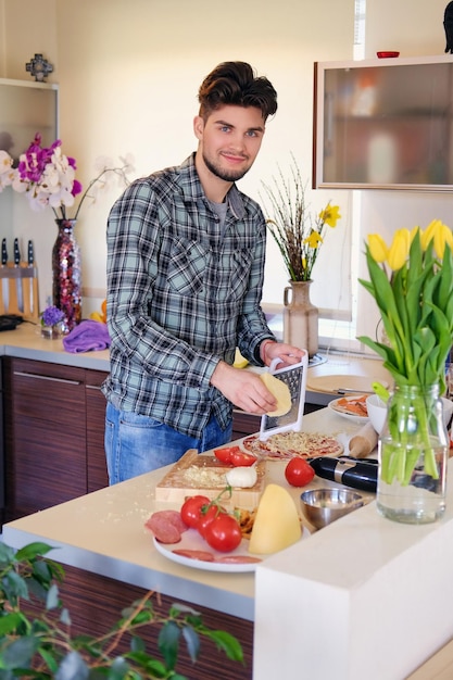 Een knappe, bebaarde man gekleed in een fleece-shirt die salade maakt van groenten in de huiskeuken.