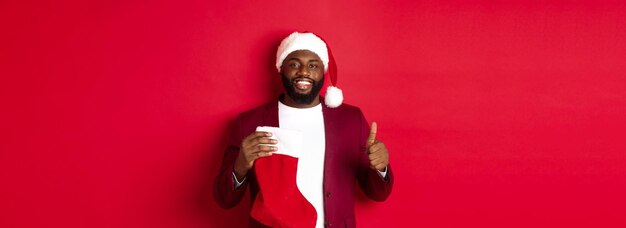 Een knappe man met een baard ontvangt een kerstcadeau in een sok met een duim omhoog en een glimlach terwijl hij tegen