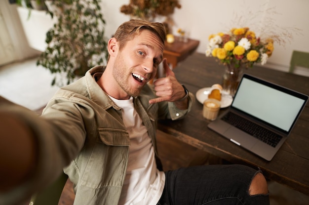 Een knappe man neemt een selfie op zijn mobiele telefoon met een laptop die laat zien dat hij de telefoon belt met een glimlach op zijn hand.