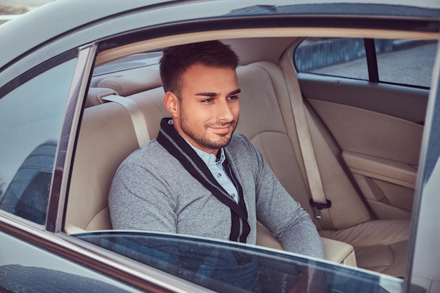 Een knappe modieuze man in elegante kleding zit in de auto.