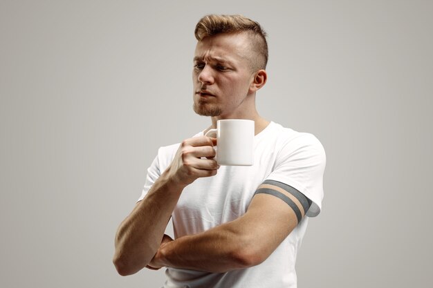 Een koffiepauze nemen. knappe jonge man met koffiekopje terwijl je tegen grijze studio staat