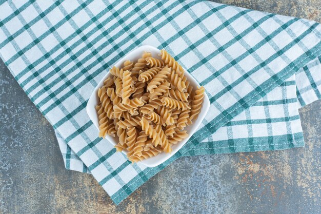 Een kom bruine fusilli pasta, op de handdoek, op het marmeren oppervlak.