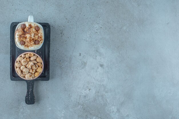 Een kom cornflakes en een kopje cappuccino op een bord, op de blauwe achtergrond.