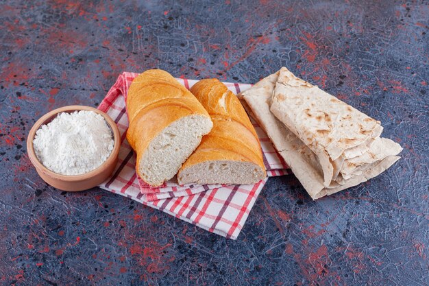 Een kom met bloem, lavash en gesneden brood op een theedoek, op het blauw.