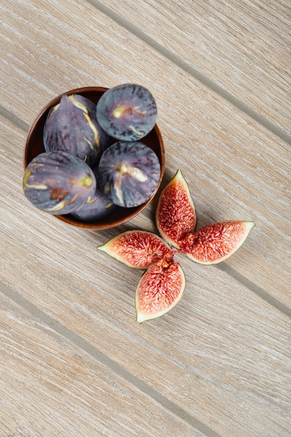 Een kom met zwarte vijgen en plakjes vijgen op een houten tafel