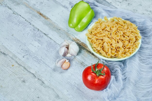 Een kom rauwe pasta met tomaat, peper en knoflook.