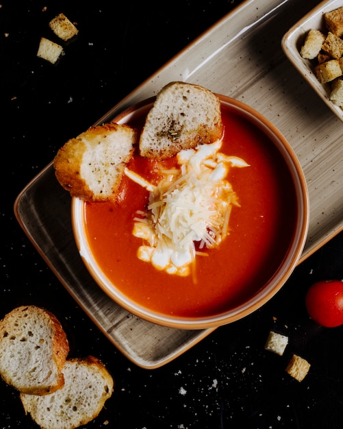 Een kom tomatensoep met gehakte kaas en broodcrackers binnen op een dienblad.