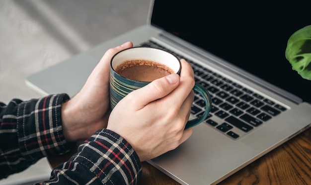 Een kopje cacao in mannelijke handen op de achtergrond van een laptop