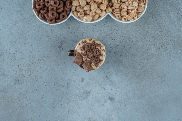 Een kopje cappuccino naast cornflakes in kommen, op de blauwe achtergrond.