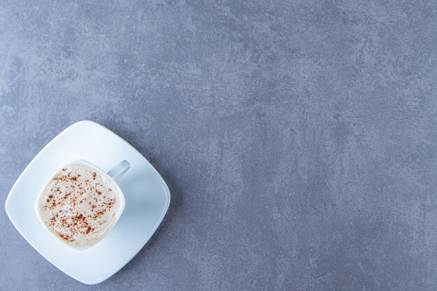 Een kopje cappuccino op een schoteltje, op de blauwe tafel.