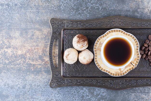 Een kopje donkere koffie met koekje op een donker bord.