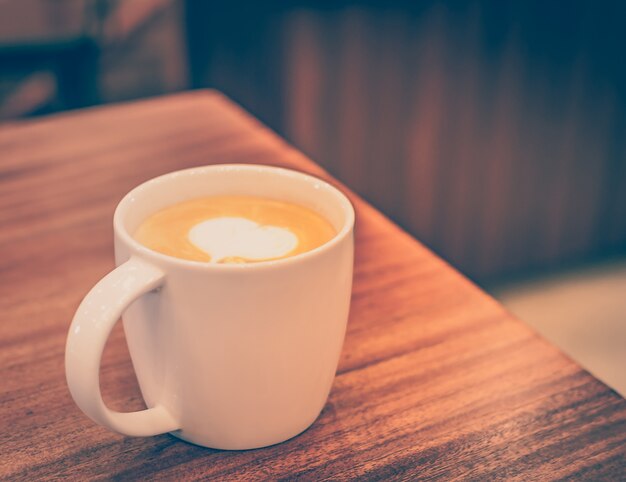 Een kopje koffie met hartpatroon in een witte kop op houten achtergrond. Uitstekende toon.