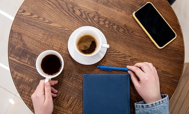 Een kopje koffie op een houten tafel en een bovenaanzicht van een notitieblok