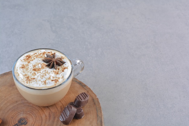 Een kopje romige koffie en kaneelstokjes op een houten bord.