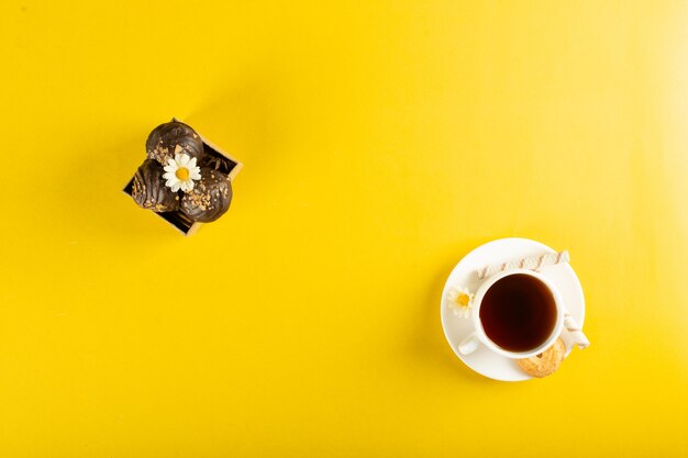 Een kopje thee met chocolade pralines op geel. bovenaanzicht