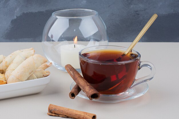 Een kopje thee met kaneel en koekjes op witte tafel.