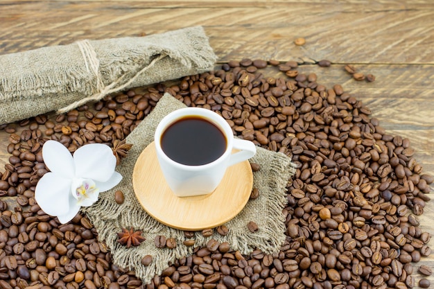 Een kopje vers bereide aromatische koffie op een houten tafel met een orchideebloem en koffiebonen. samenstelling van koffie in de ochtend op het platteland.