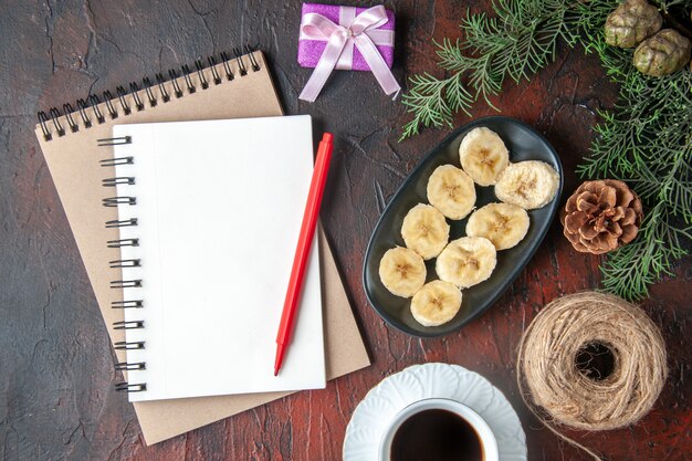 Een kopje zwarte thee spar takken decoratie accessoires en cadeau en notitieboekje met pen en gehakte banaan op donkere achtergrond