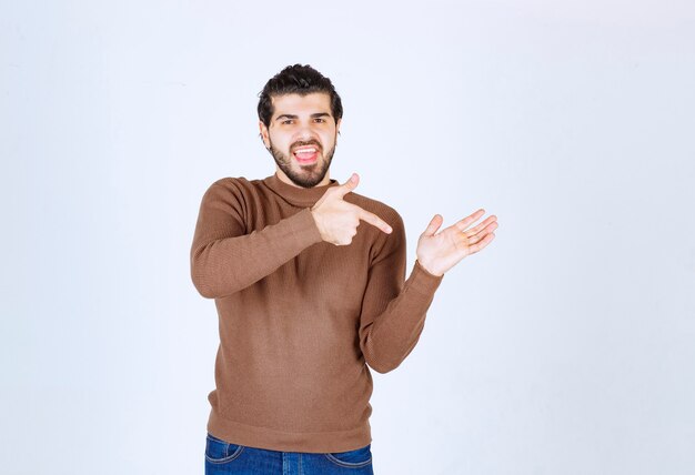 Een lachend jongemanmodel met een bruine trui die naar zijn handpalm wijst. Hoge kwaliteit foto