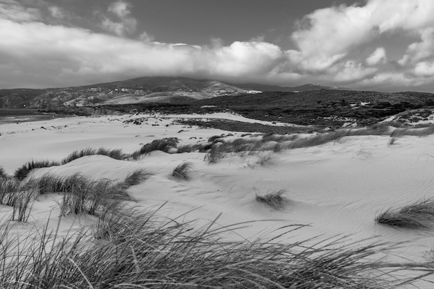 Een landschap met gras bedekt met zand omgeven door bergen onder de storm wolken
