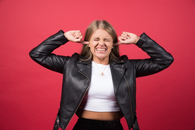 Een langharige mooie jonge vrouw die haar oren bedekt met haar handen