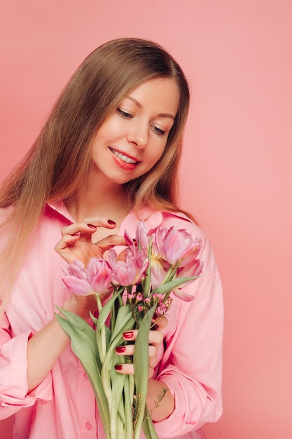 Een lieve charmante vrouw met bloemen in een roze jurk op een roze achtergrond lacht geluk en geluk