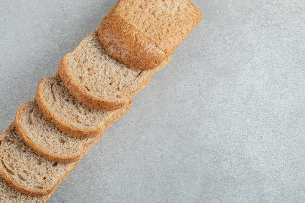 Een lijn van sneetjes bruin brood op een grijze achtergrond.