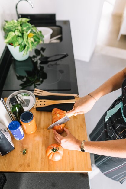 Een luchtmening van vrouwen scherpe plakken van tomaat op keukenteller