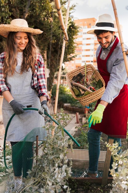 Een man die de glimlachende vrouwelijke tuinman leidt die de plant water geeft met een groene slang