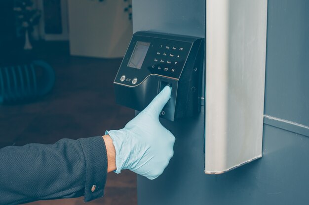 een man die de intercom laat lezen om zijn vingerafdruk te lezen om de deur te openen met handschoenen aan.