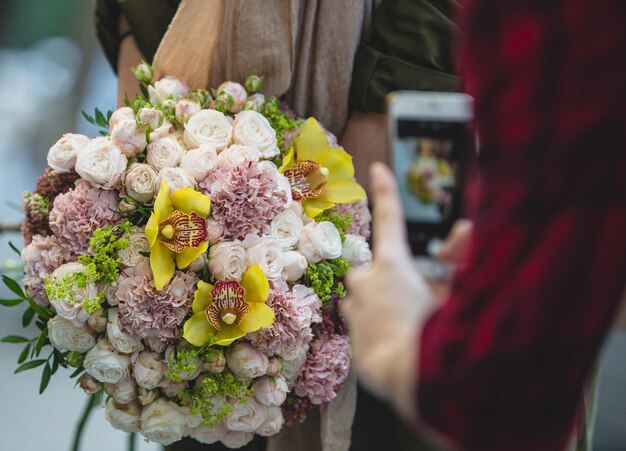Een man die met telefoon een prachtig wit en paars bruidsboeket fotografeert