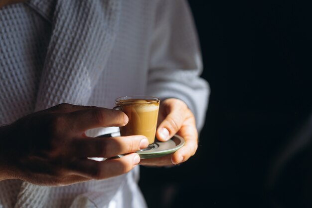 Een man in een badjas houdt een kleine mok koffie vast