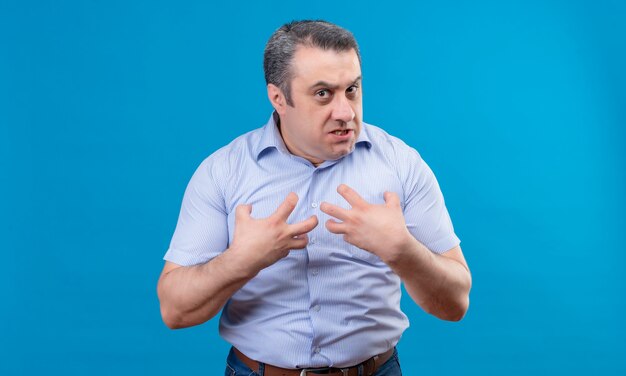 Een man in een blauw shirt toont emotioneel agressie en woede met de handen op zichzelf wijzend op een blauwe ruimte