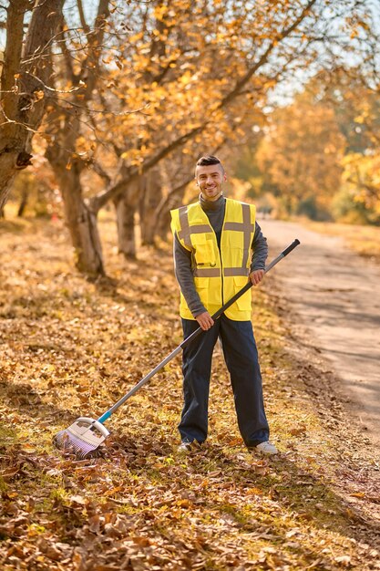 Een man in een geel vest die bladeren harkt in het park