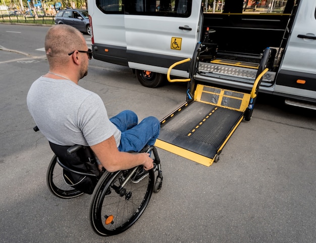 Een man in een rolstoel gaat naar de lift van een speciaal voertuig voor mensen met een handicap.