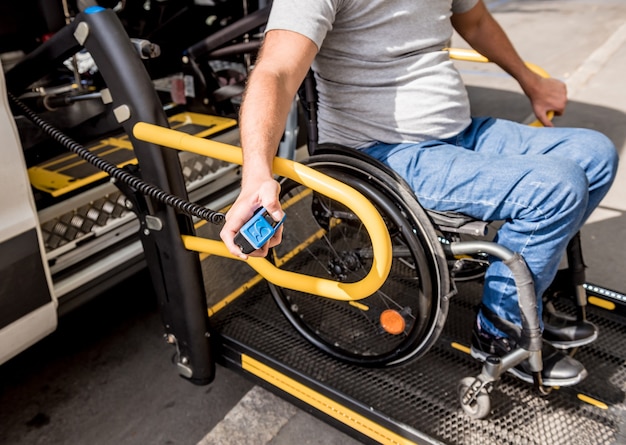 Een man in een rolstoel op een lift van een voertuig voor mensen met een handicap.