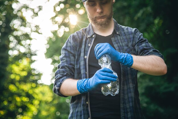 Een man in handschoenen met een plastic fles in zijn handen maakt het bos schoon
