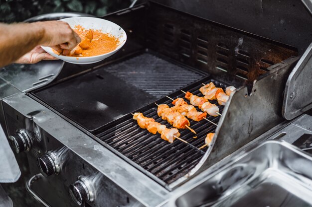 Een man in tatoeages maakt barbecue vlees buiten.