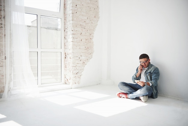 Gratis foto een man in vrijetijdskleding zit thuis in een leeg appartement en belt aan de telefoon.