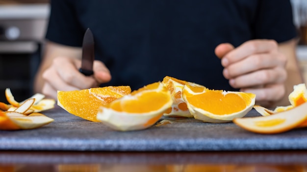 Een man met gesneden sinaasappel op een kookplank en een mes in zijn handen