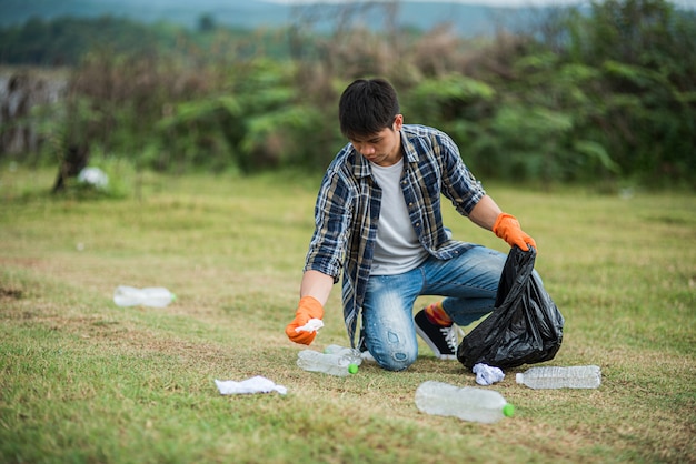 Een man met oranje handschoenen die vuilnis in een zwarte zak verzamelen.