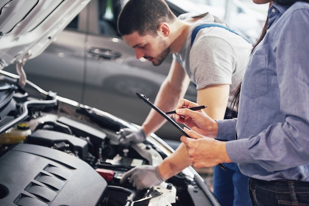 Een man monteur en vrouw klant kijken naar de motorkap en bespreken reparaties