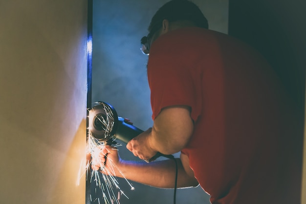 Een man repareert een metalen deur in de kelder van zijn huis met behulp van een handmatige slijpmachine.